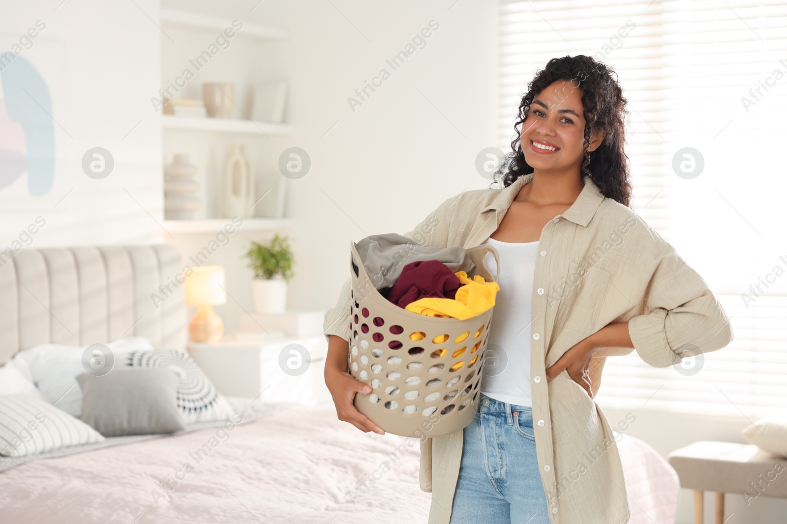 Photo of Happy woman with basket full of laundry in bedroom