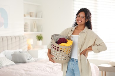 Happy woman with basket full of laundry in bedroom