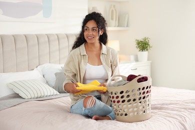 Photo of Happy woman with basket full of laundry on bed at home