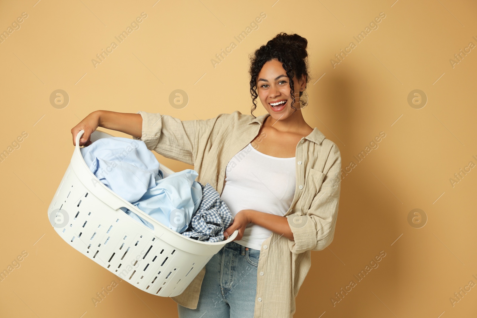 Photo of Happy woman with basket full of laundry on beige background