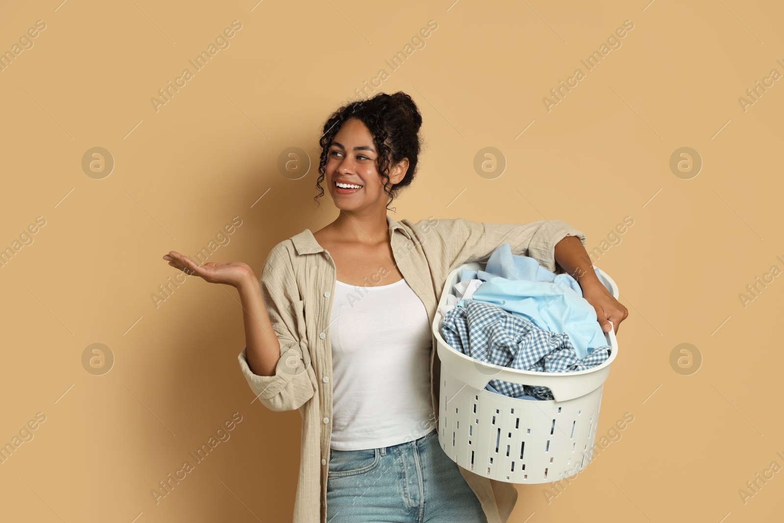 Photo of Happy woman with basket full of laundry on beige background