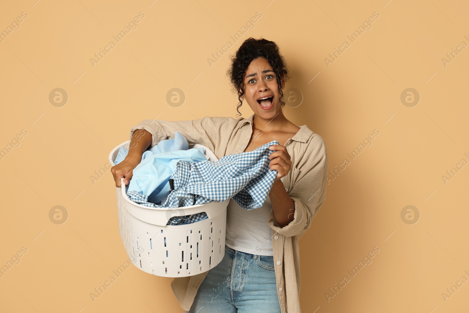 Photo of Shocked woman with basket full of laundry on beige background