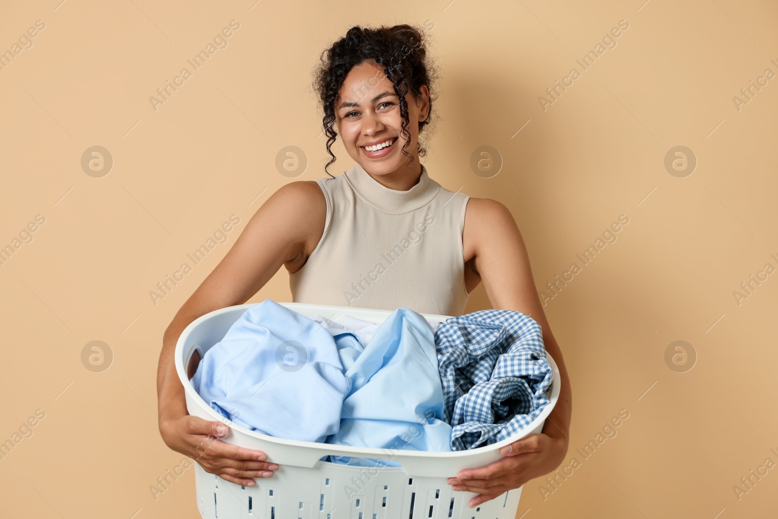 Photo of Happy woman with basket full of laundry on beige background