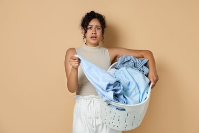 Displeased woman with basket full of laundry on beige background