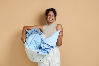 Photo of Happy woman with basket full of laundry on beige background, space for text