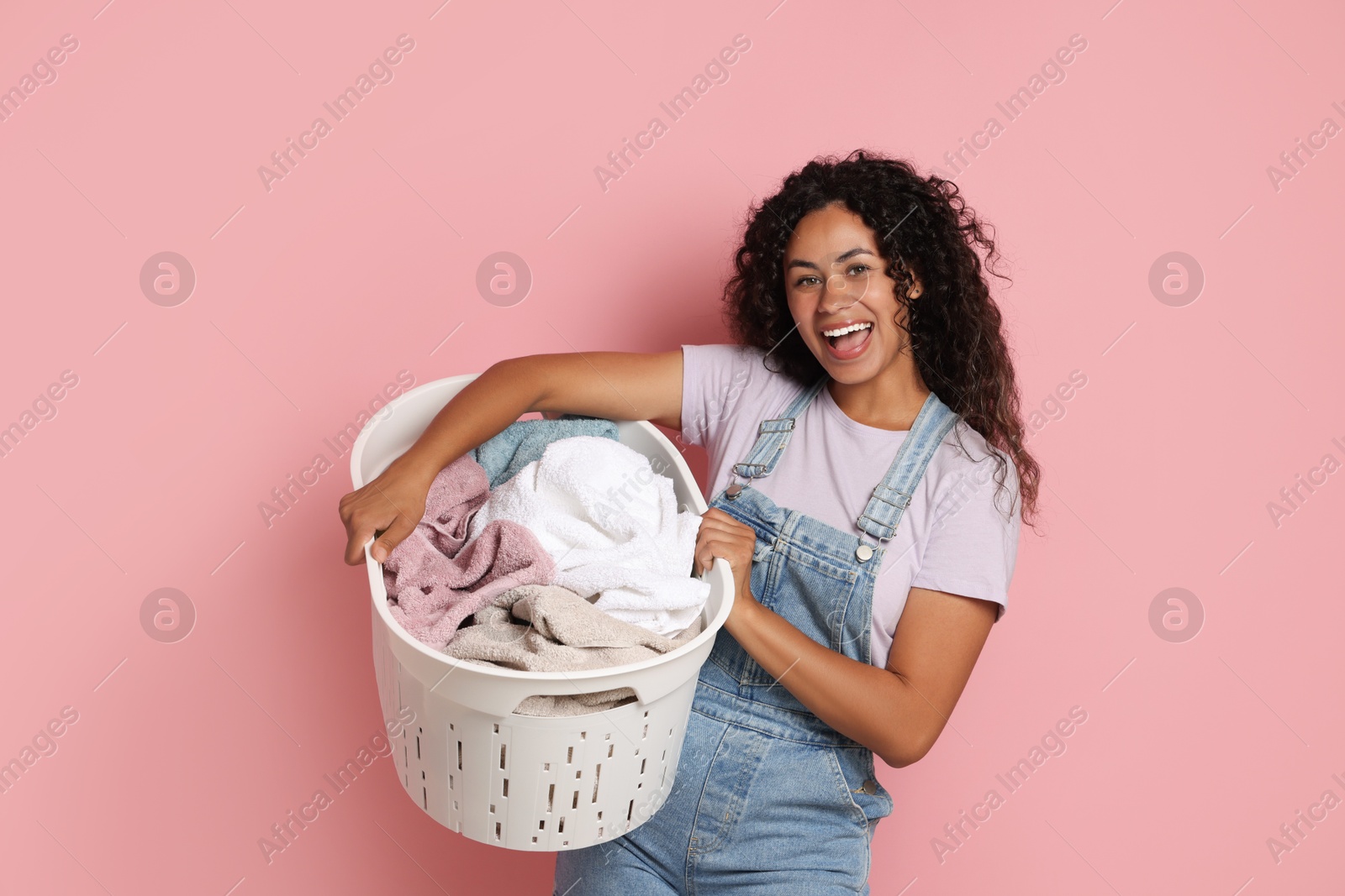 Photo of Happy woman with basket full of laundry on pink background