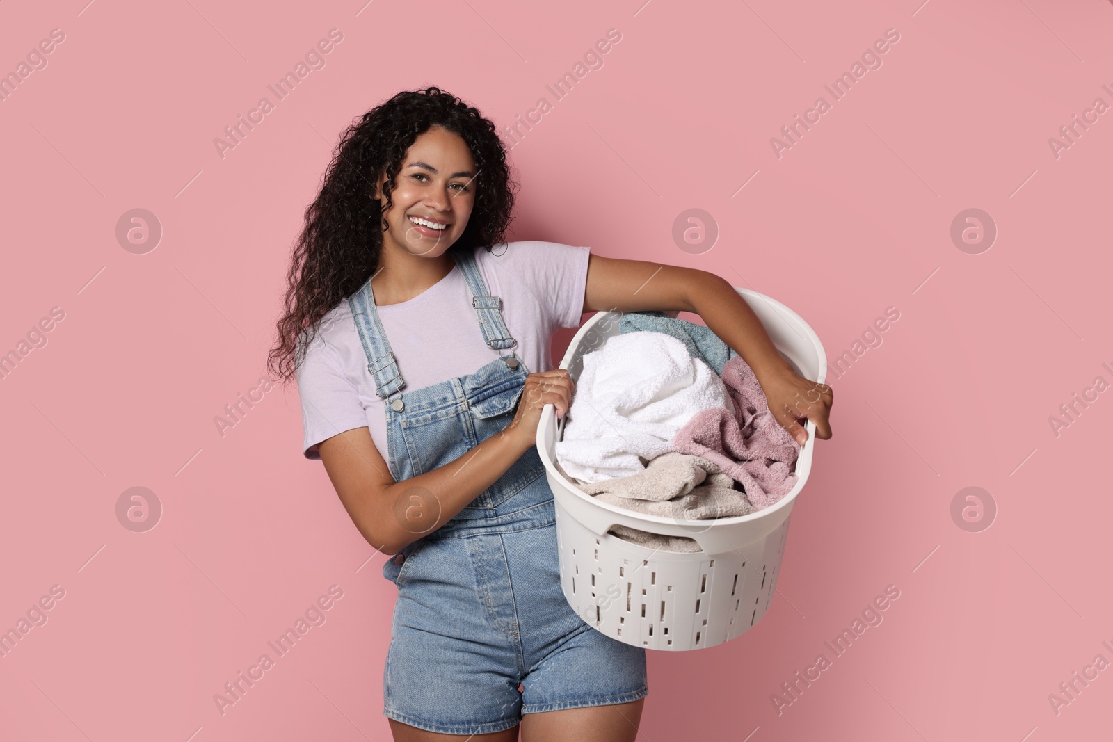 Photo of Happy woman with basket full of laundry on pink background