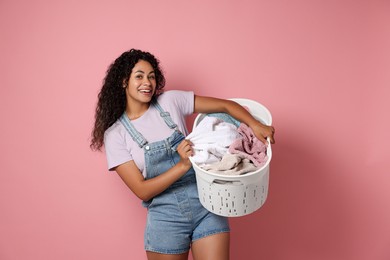 Photo of Happy woman with basket full of laundry on pink background