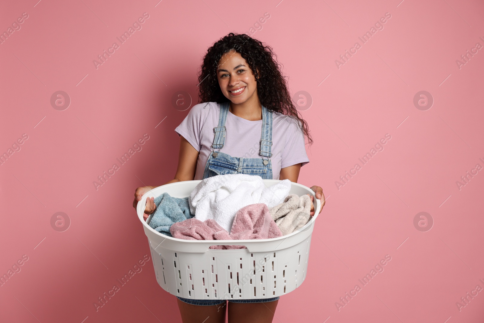 Photo of Happy woman with basket full of laundry on pink background