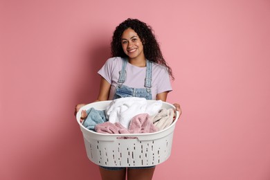 Happy woman with basket full of laundry on pink background