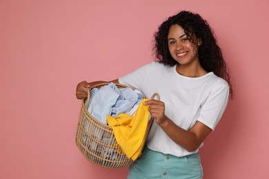 Photo of Happy woman with basket full of laundry on pink background, space for text