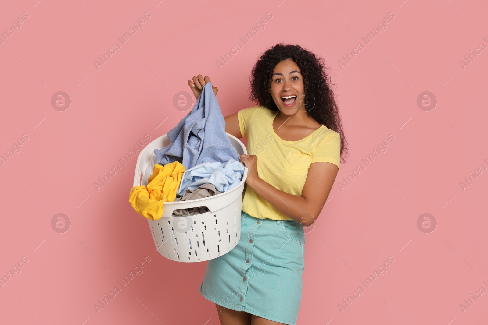 Photo of Happy woman with basket full of laundry on pink background