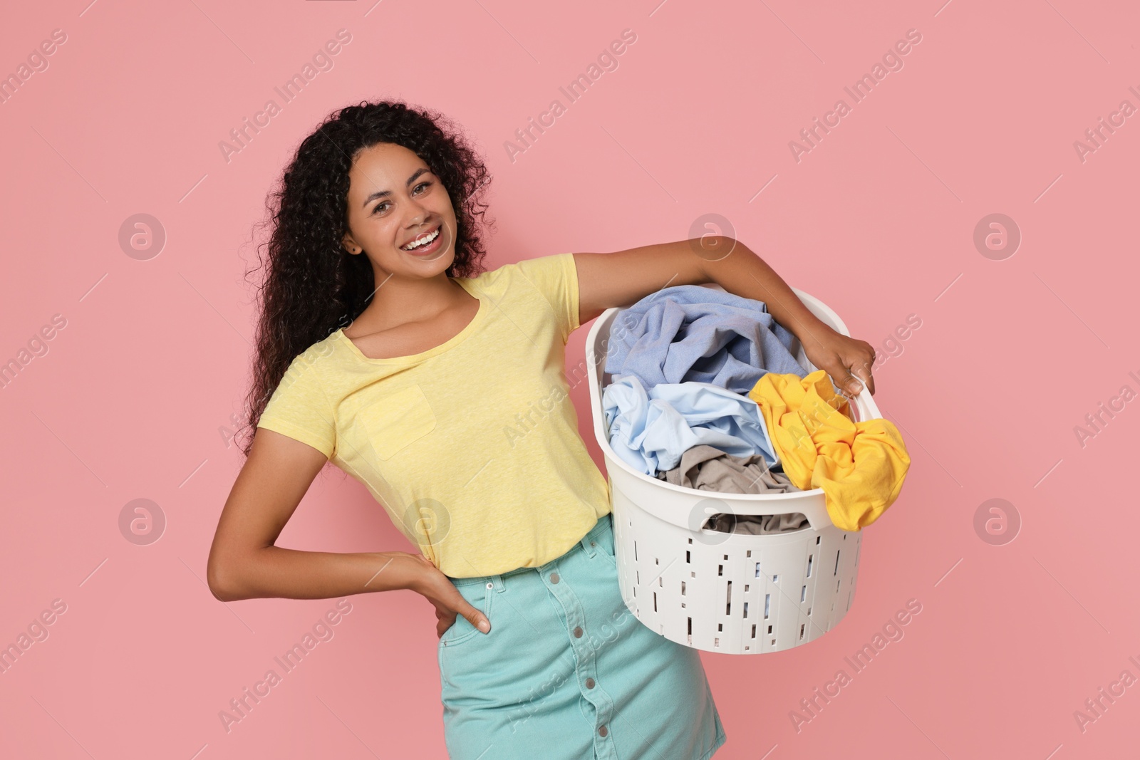 Photo of Happy woman with basket full of laundry on pink background