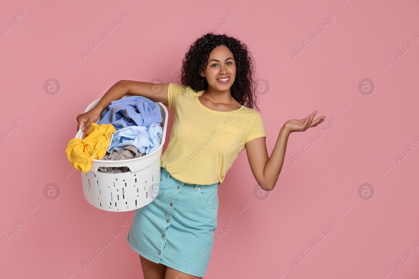 Photo of Happy woman with basket full of laundry on pink background