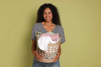 Happy woman with basket full of laundry on olive background