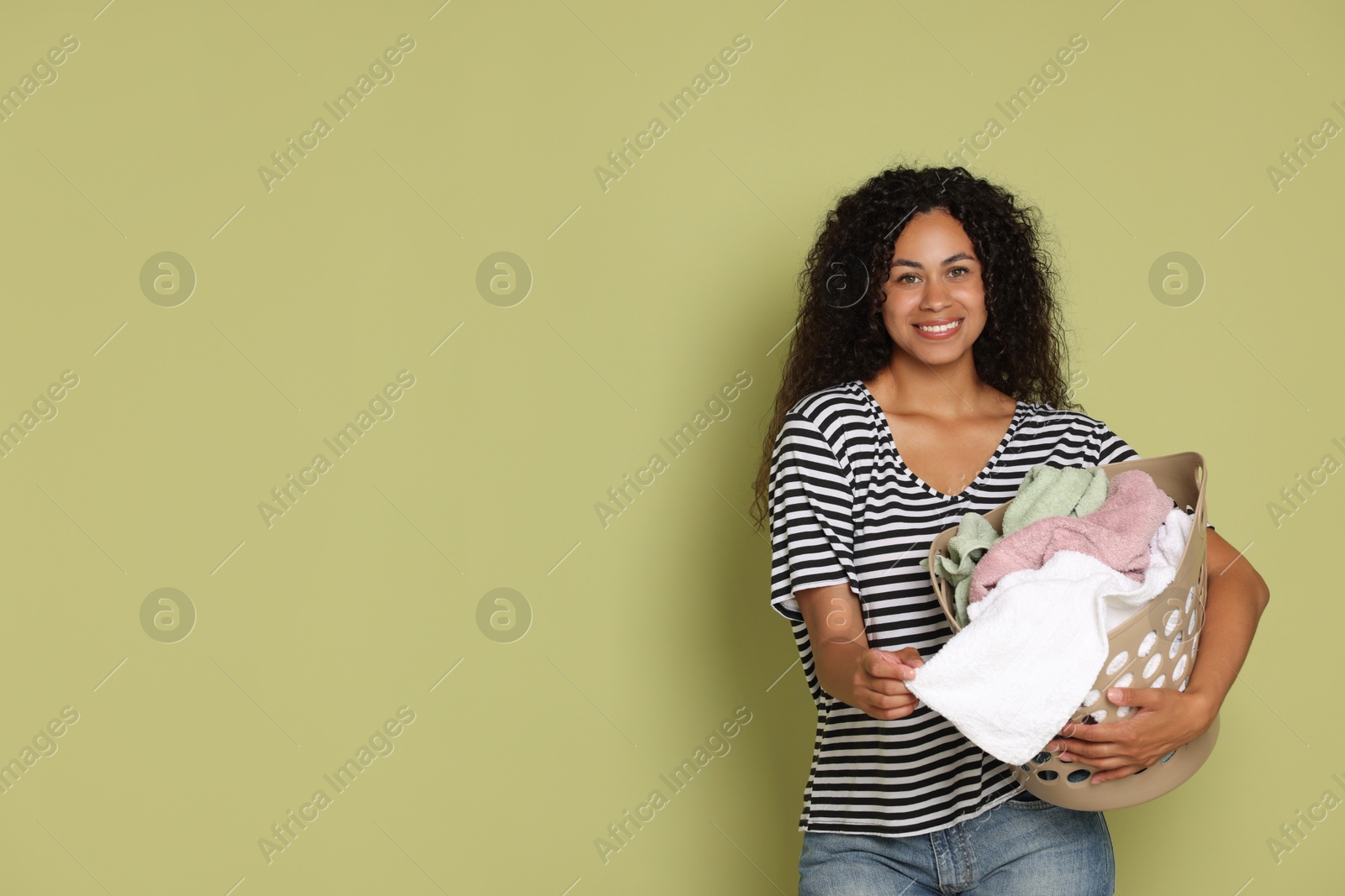 Photo of Happy woman with basket full of laundry on olive background, space for text