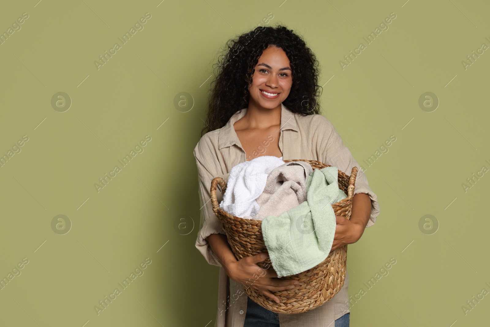 Photo of Happy woman with basket full of laundry on olive background