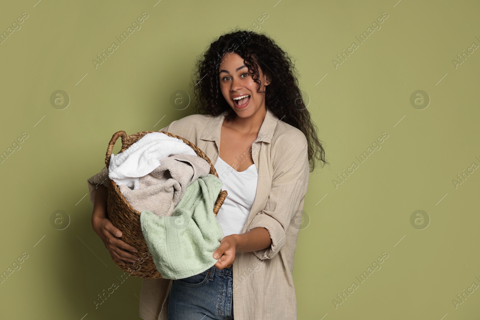 Photo of Happy woman with basket full of laundry on olive background, space for text