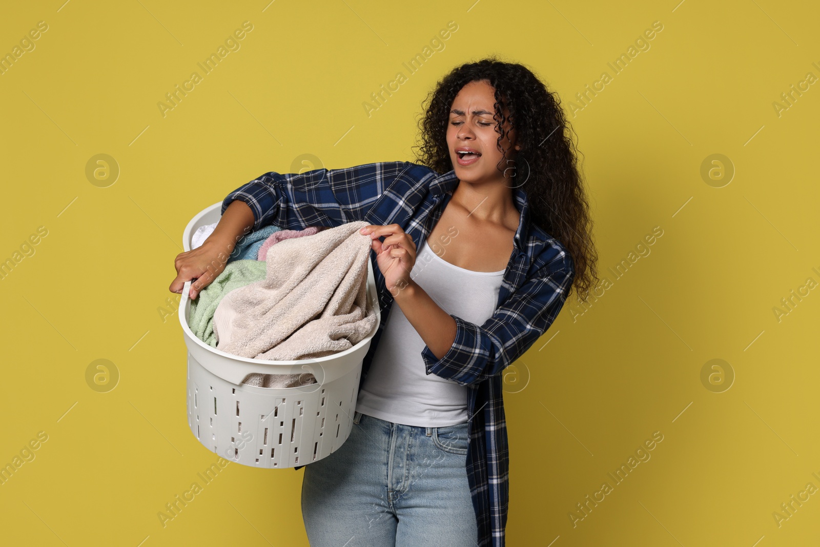 Photo of Emotional woman with basket full of laundry on yellow background