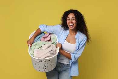 Photo of Happy woman with basket full of laundry on yellow background