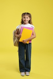 Positive girl with backpack and books on yellow background