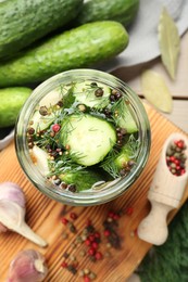 Photo of Making pickles. Fresh cucumbers and spices in jar on wooden table, top view