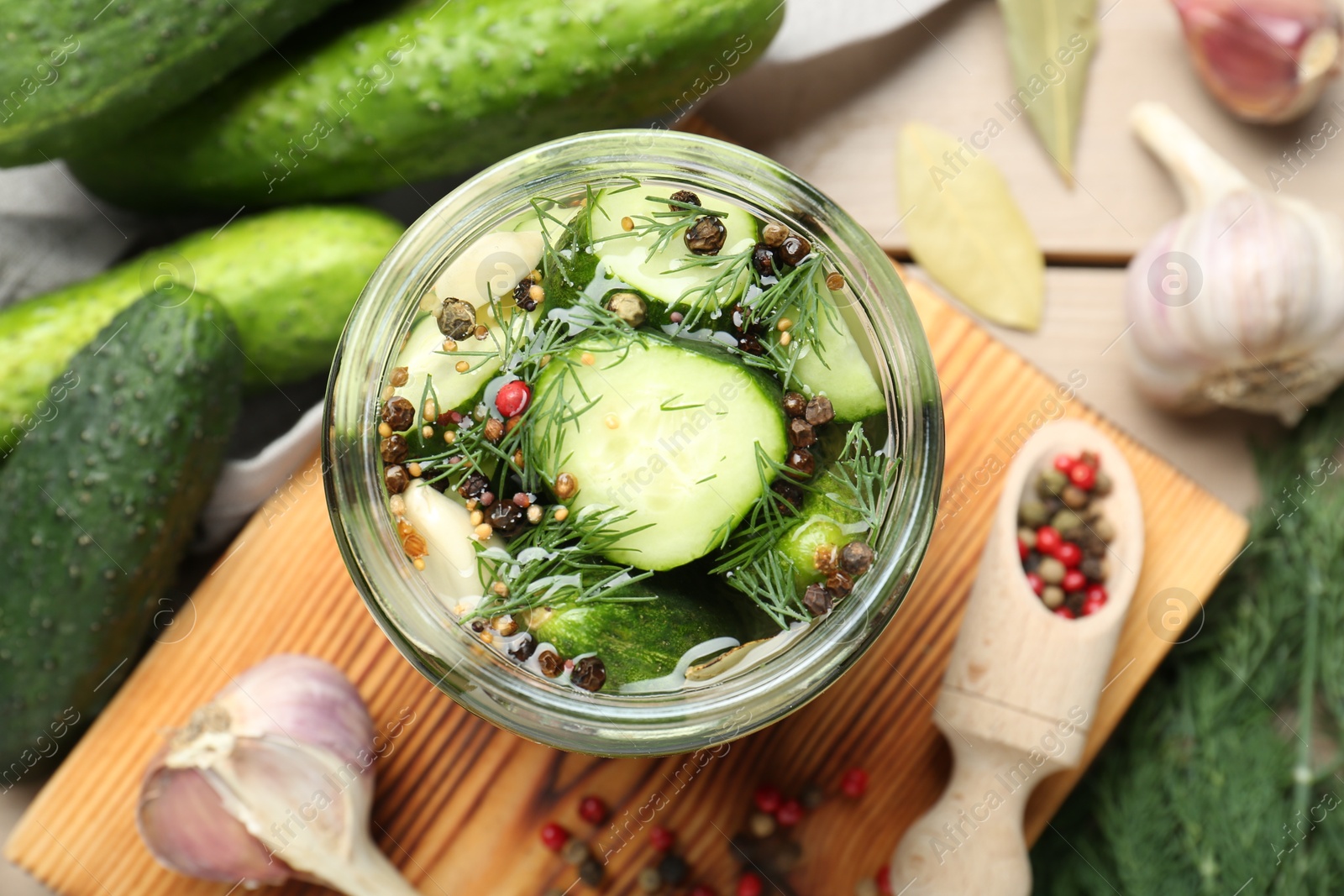 Photo of Making pickles. Fresh cucumbers and spices in jar on wooden table, top view