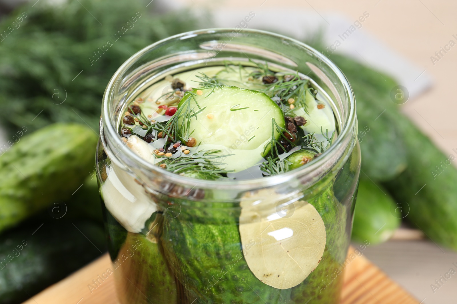 Photo of Making pickles. Fresh cucumbers and spices in jar on wooden table, closeup