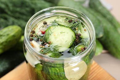 Photo of Making pickles. Fresh cucumbers and spices in jar on wooden table, closeup