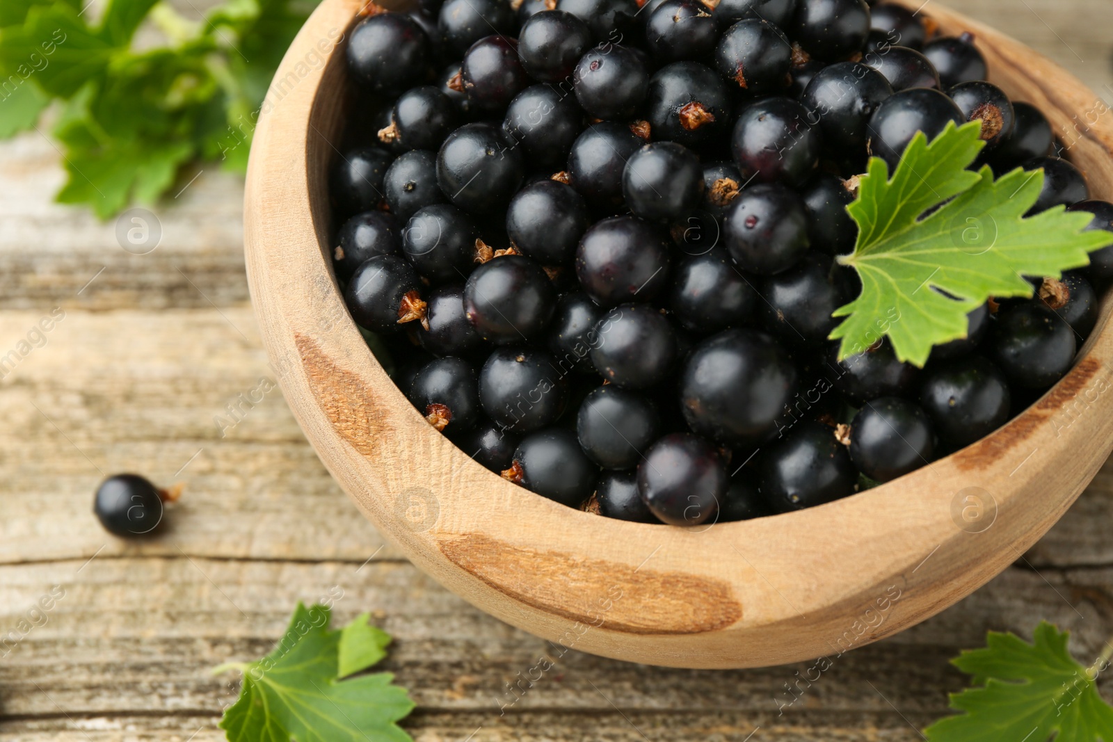 Photo of Ripe black currants and leaves in bowl on wooden table, closeup