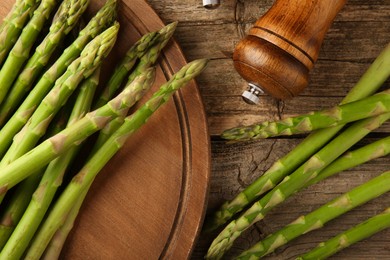 Photo of Board with fresh green asparagus stems and shakers on wooden table, flat lay