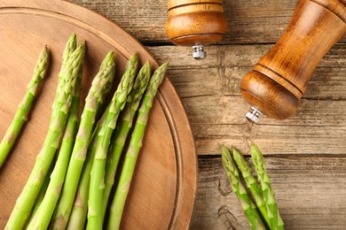 Photo of Board with fresh green asparagus stems and shakers on wooden table, flat lay