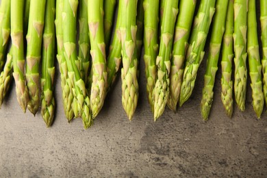 Photo of Fresh green asparagus stems on grey textured table, flat lay. Space for text