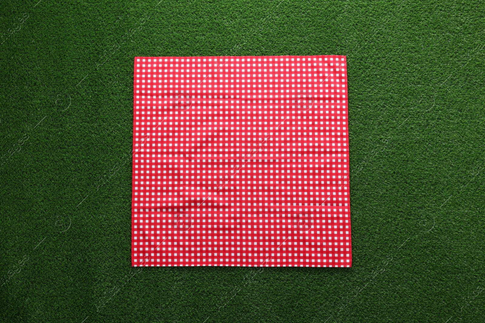 Red checkered picnic tablecloth on green grass, top view Photo of Red checkered picnic tablecloth on green grass, top view