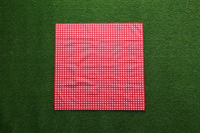 Photo of Red checkered picnic tablecloth on green grass, top view