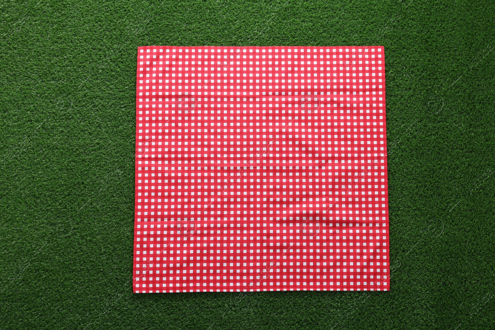Photo of Red checkered picnic tablecloth on green grass, top view