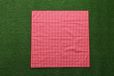 Photo of Red checkered picnic tablecloth on green grass, top view