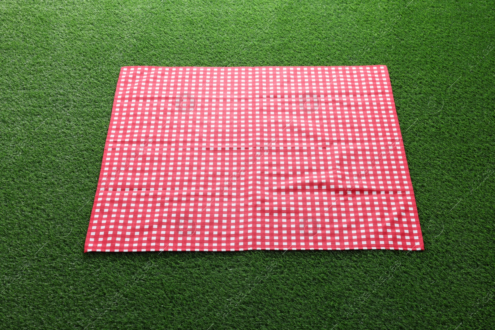 Photo of Red checkered picnic tablecloth on green grass