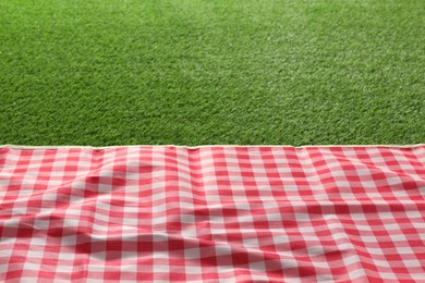 Photo of Checkered picnic tablecloth on green grass, closeup. Space for text