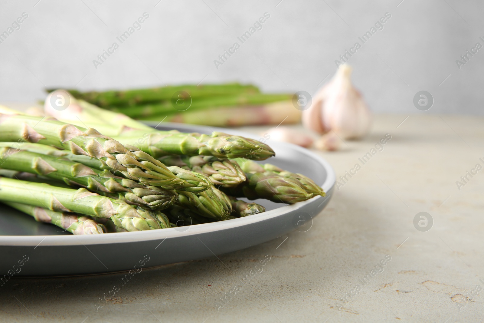 Photo of Fresh green asparagus stems on gray table, closeup. Space for text