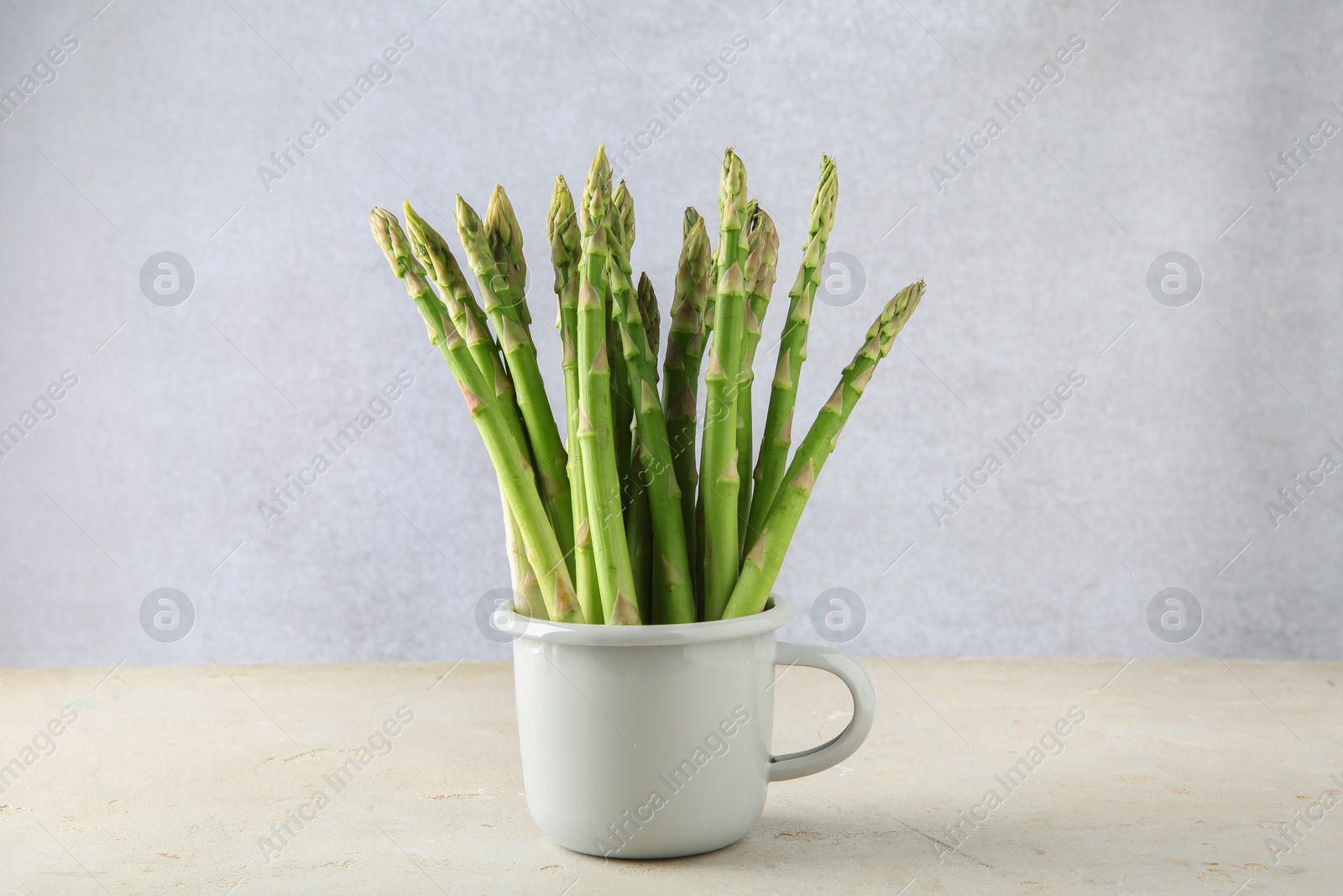 Photo of Fresh green asparagus stems in cup on gray table