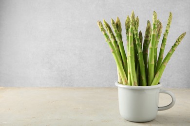 Photo of Fresh green asparagus stems in cup on gray table, space for text