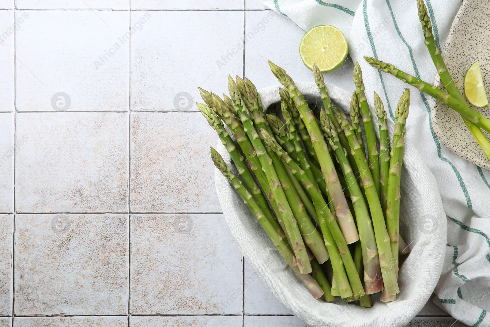 Photo of Fresh green asparagus stems and lime on light textured tiled table, flat lay. Space for text