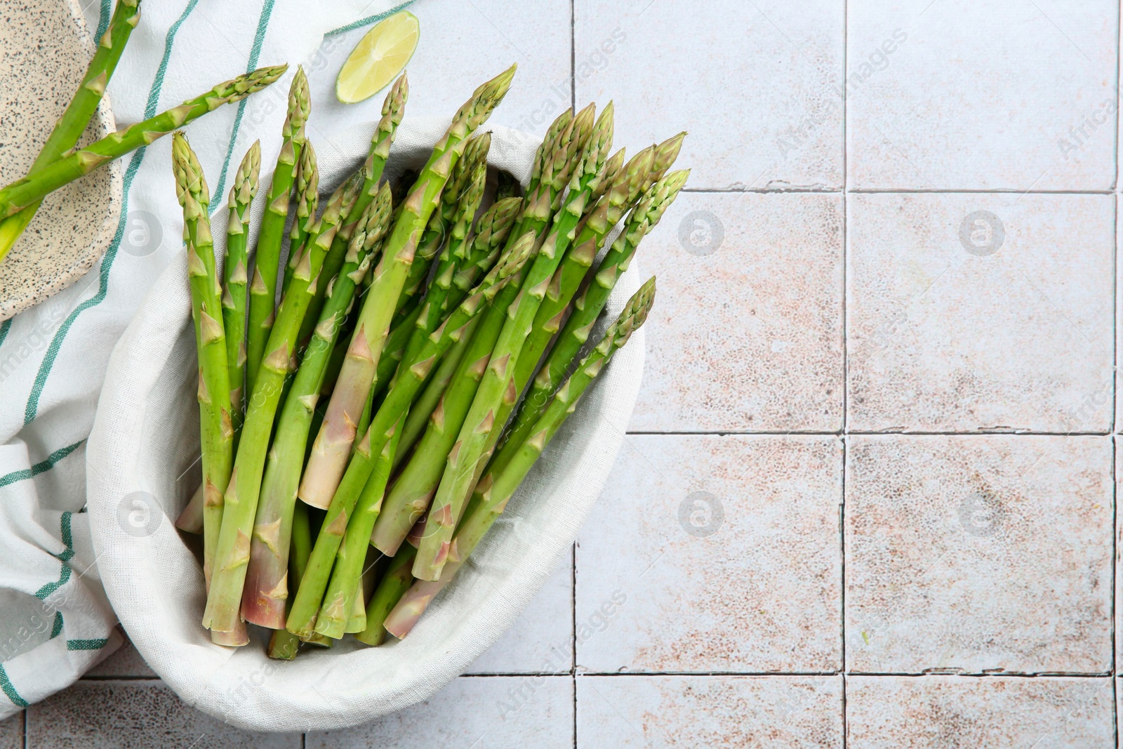 Photo of Fresh green asparagus stems and lime on light textured tiled table, flat lay. Space for text