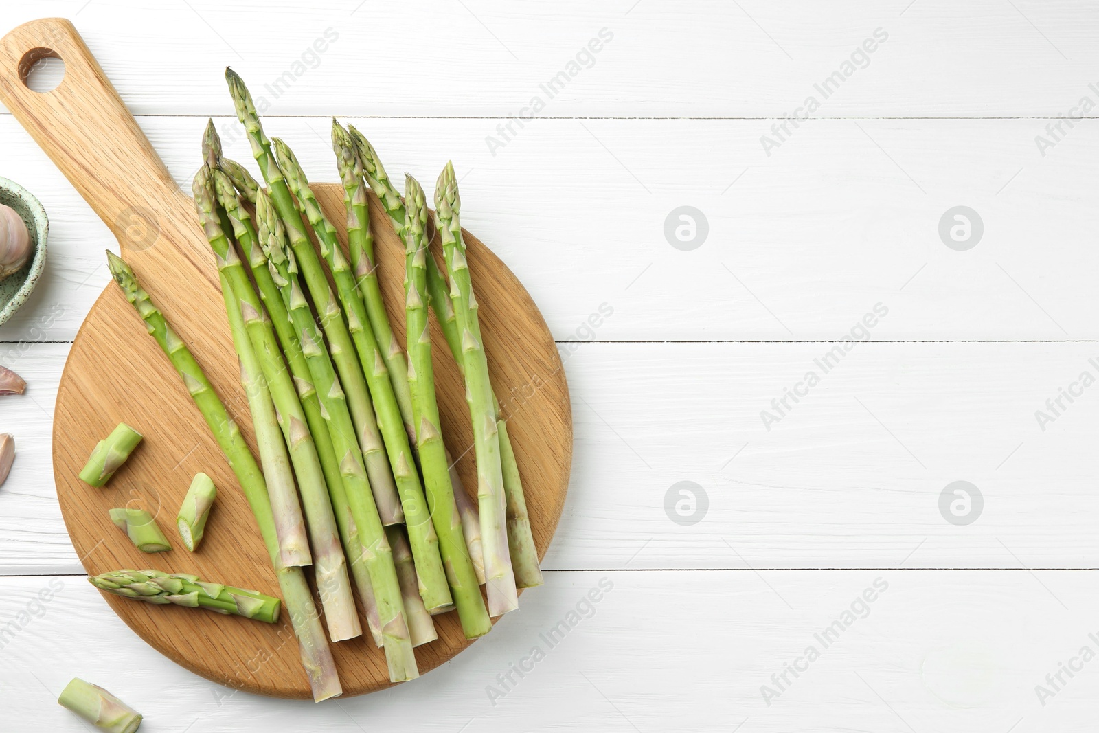 Photo of Fresh green asparagus stems and garlic on white wooden table, flat lay. Space for text