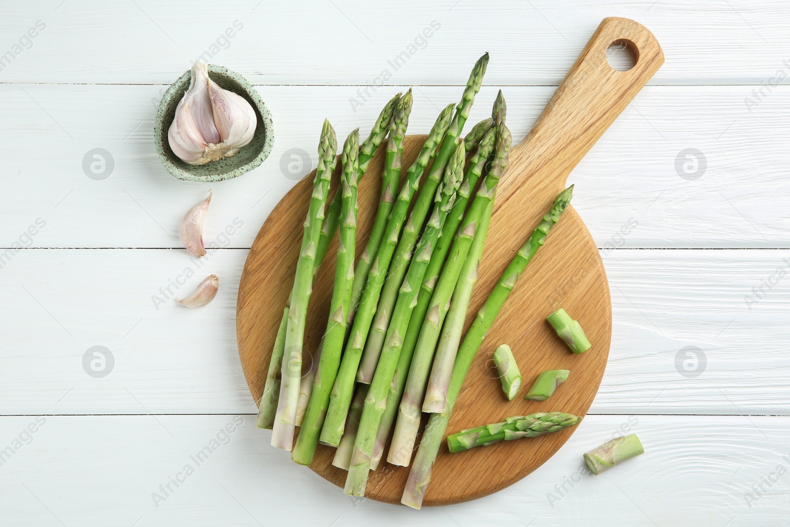 Photo of Fresh green asparagus stems and garlic on white wooden table, flat lay