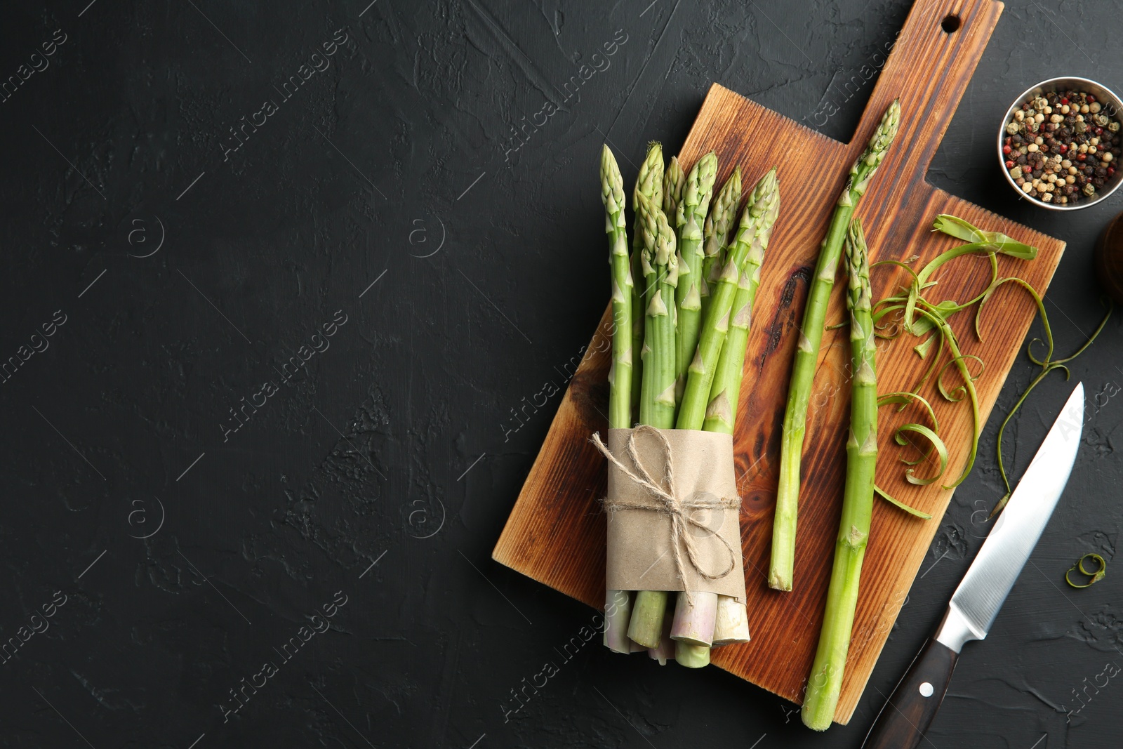 Photo of Fresh green asparagus stems, spices and knife on gray textured table, flat lay. Space for text