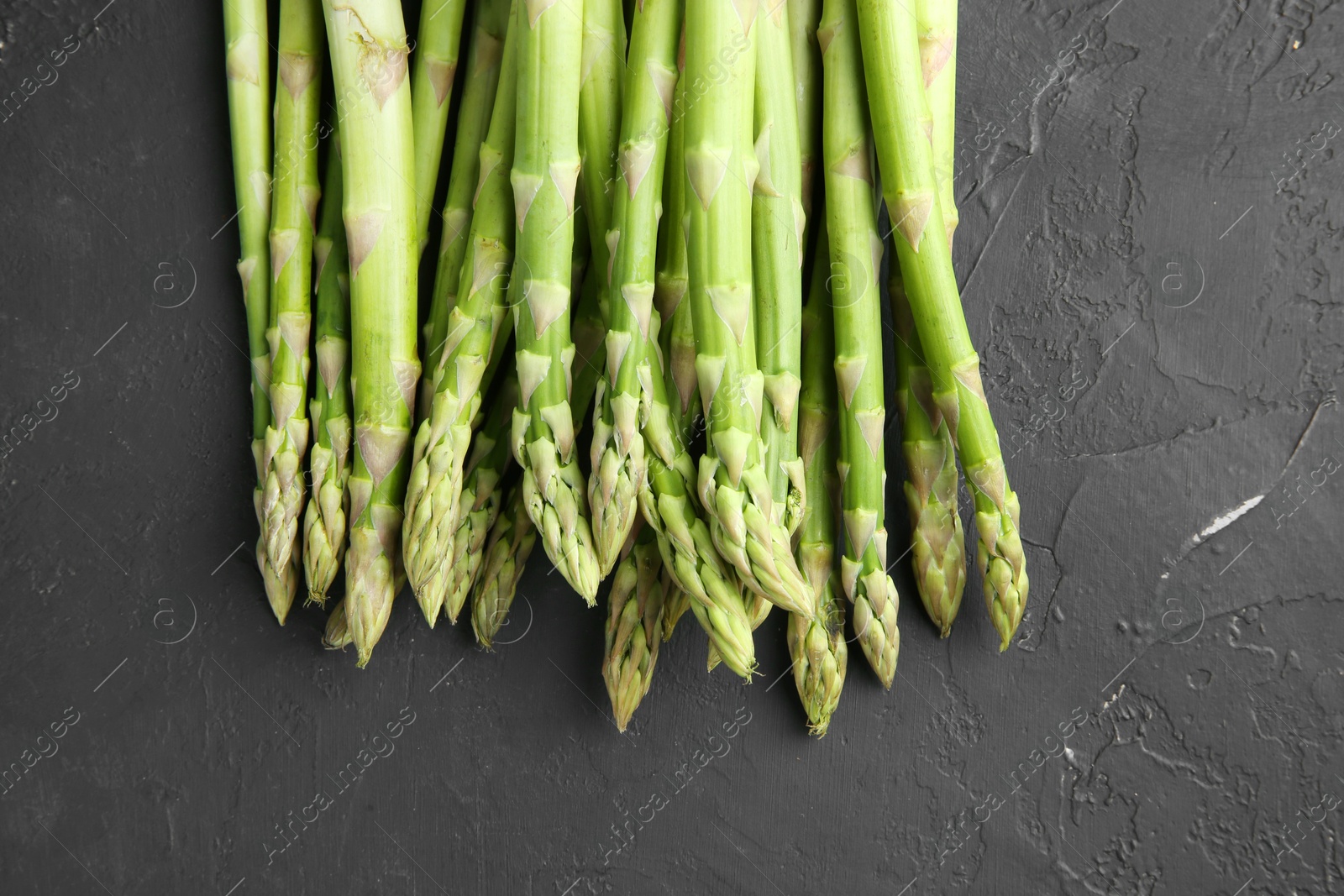 Photo of Fresh green asparagus stems on gray textured table, top view