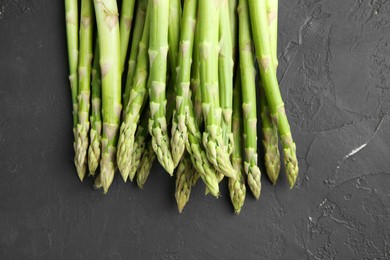 Photo of Fresh green asparagus stems on gray textured table, top view