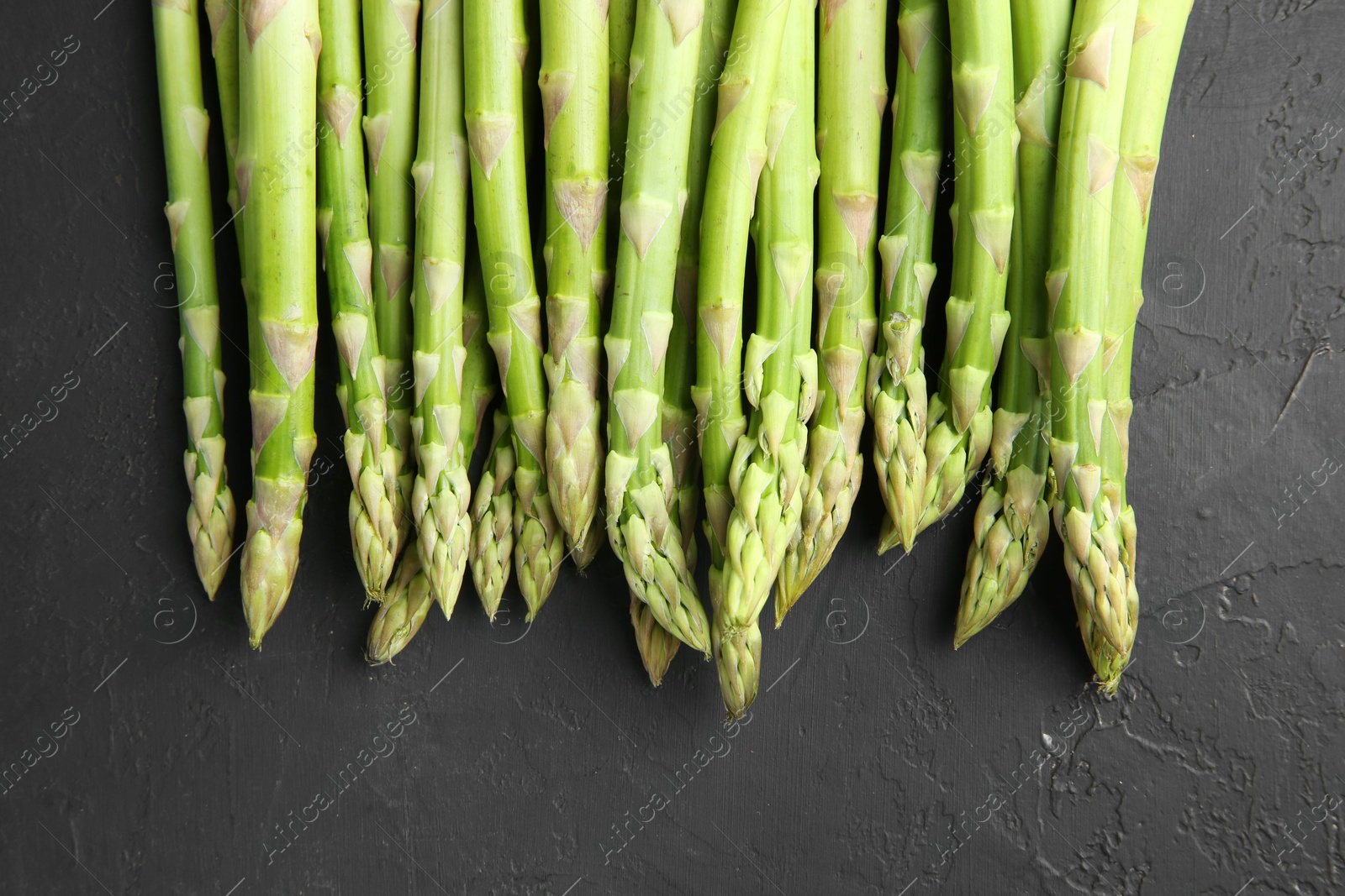 Photo of Fresh green asparagus stems on gray textured table, top view